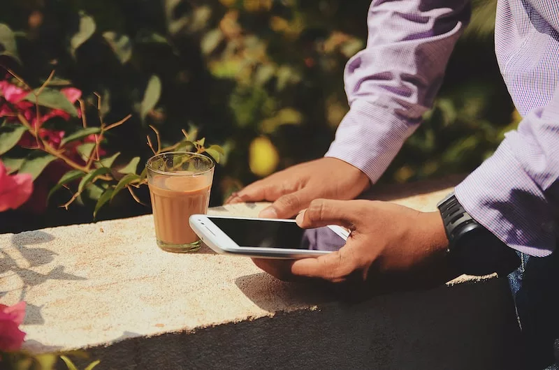 homme utilisant un smartphone à côté d'un verre dans un jardin